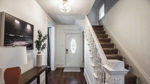 A hallway with a wooden floor, a white door, a staircase with white balusters, and a framed picture on the wall. - FarnamFieldhouse+HotTub+EpicGameRoom+FirePit+Mural (Omaha)