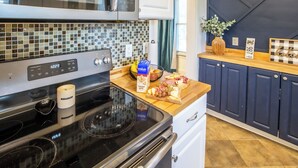 A modern kitchen with a black stove, a microwave, and a tiled backsplash. There is a wooden countertop with a bowl of fruit, a box of crackers, and a vase with green leaves. - FarnamFieldhouse+HotTub+EpicGameRoom+FirePit+Mural (Omaha)