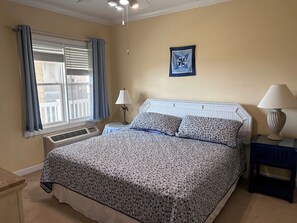 A bedroom with a bed, a window with curtains, a wall-mounted picture, and a bedside table with a lamp. - Islander Villa Condo / Oceanfront Views! Sleeps 12 By Williamson Realty (Ocean Isle Beach)