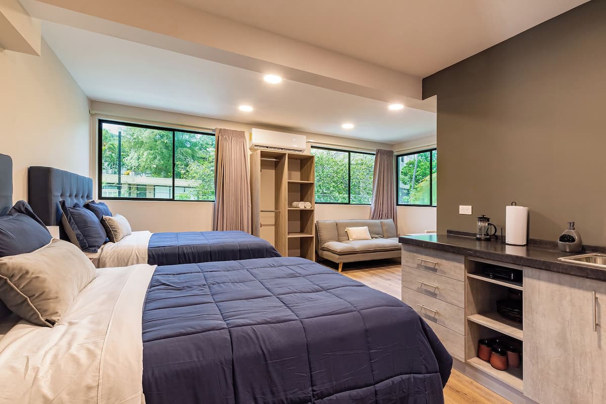 Quarto moderno com duas camas, armário embutido, área de estar e kitchenette.