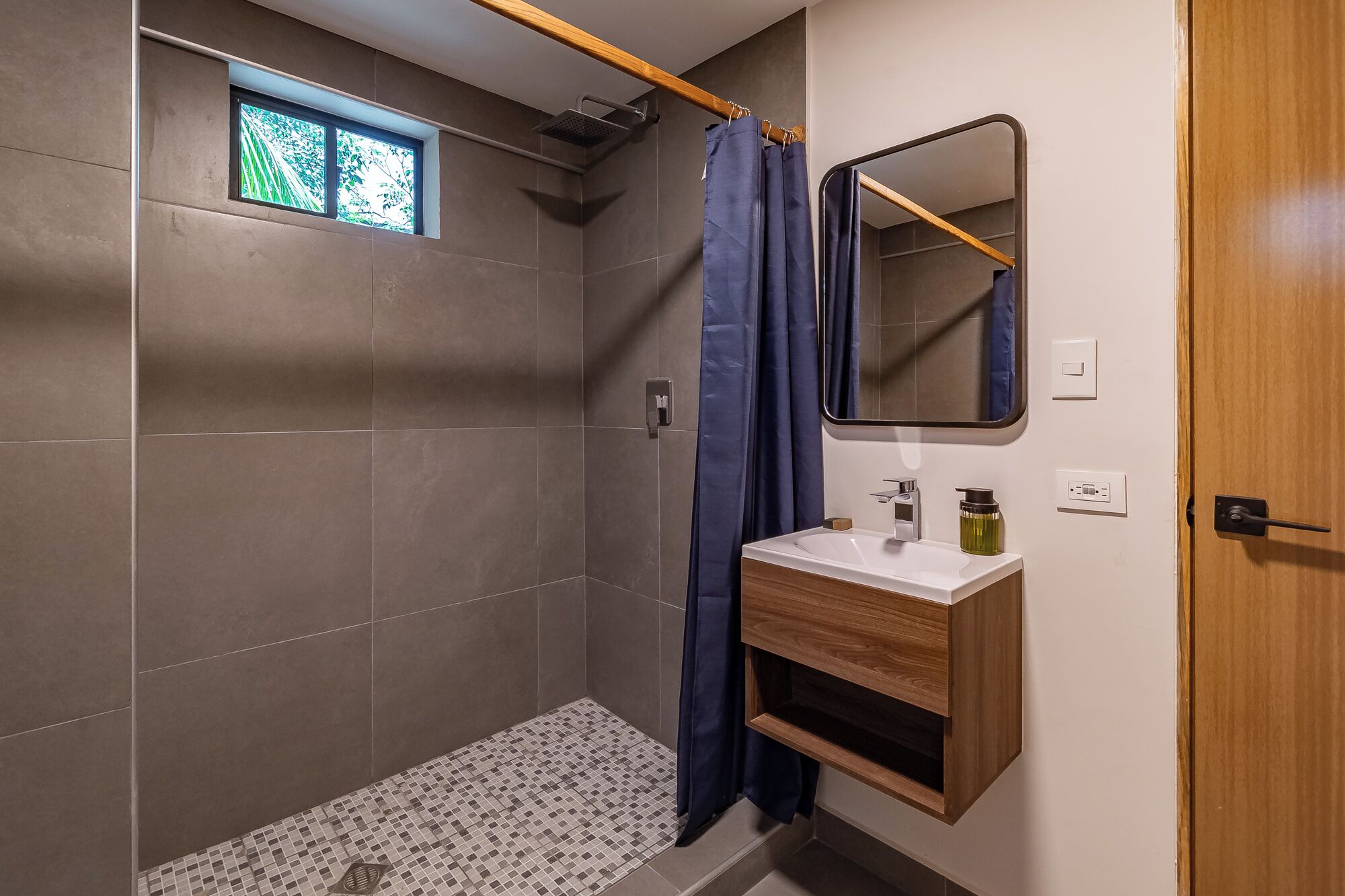 A modern bathroom with a shower, a window, a sink with a mirror, and a wooden cabinet.