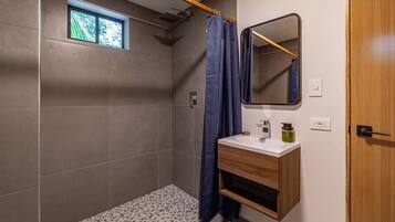 A modern bathroom with a shower, a window, a sink with a mirror, and a wooden cabinet.