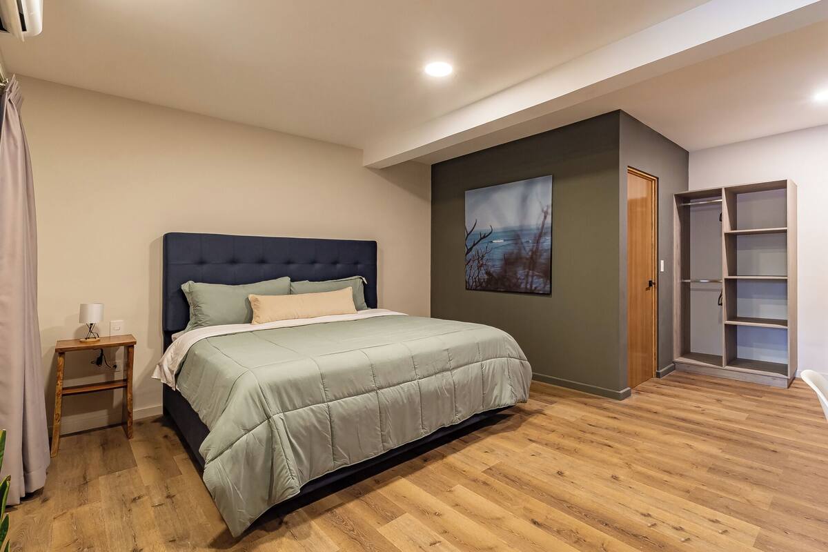 Quarto com cama, mesa de cabeceira, quadro, guarda-roupa e porta.