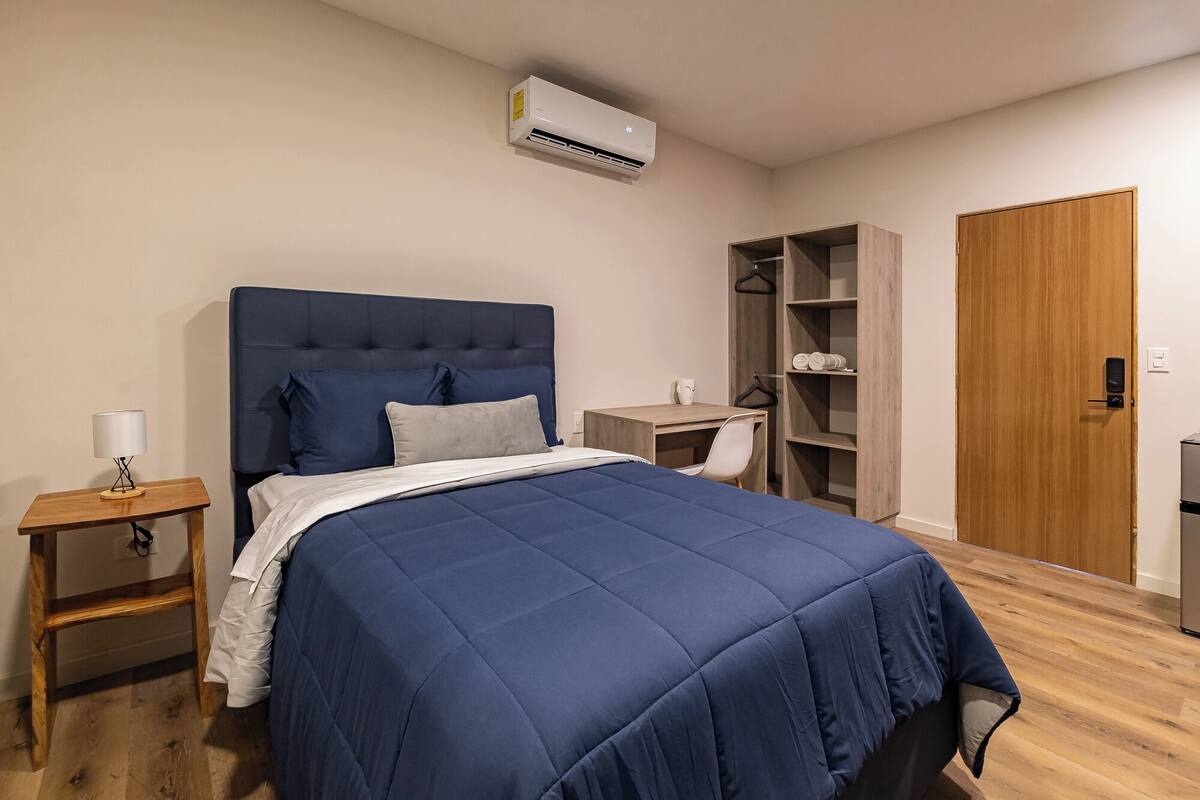 Quarto com cama, mesa de cabeceira, luminária, guarda-roupa e escrivaninha.