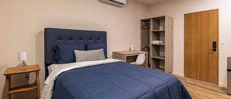 A bedroom with a bed, bedside table, lamp, wardrobe, and a desk.