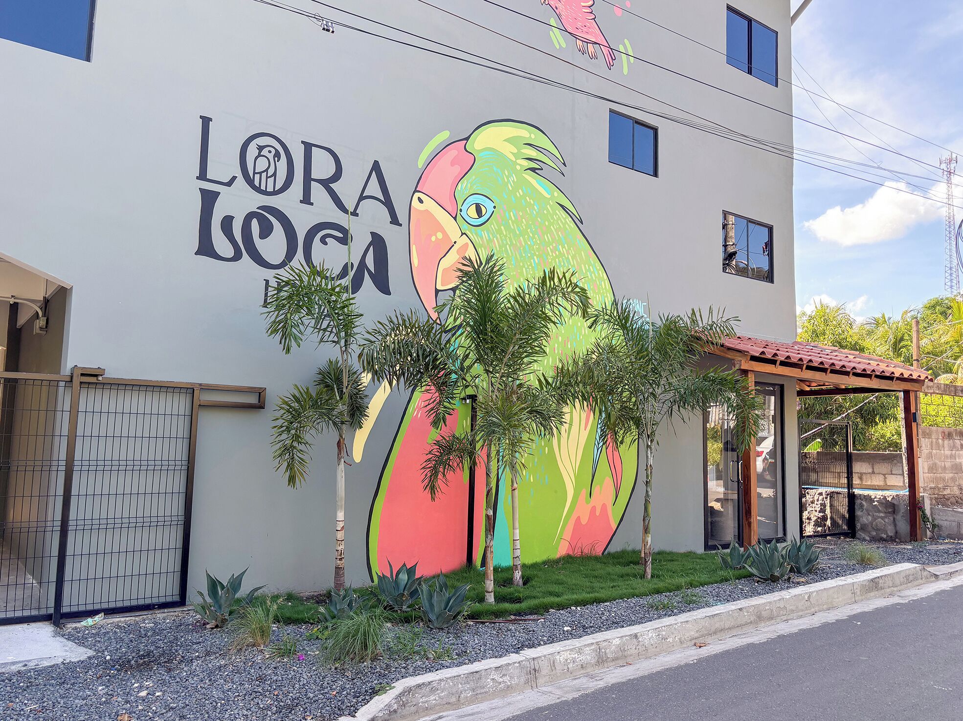 En bygning med et muralmaleri af en farverig papegøje og teksten "LORA LOCA".