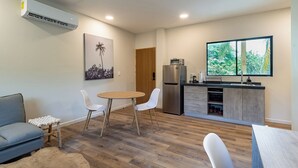 A compact living space with a dining area, kitchenette, and a large window offering a view of greenery. - Lora Loca Inn (El Zonte)