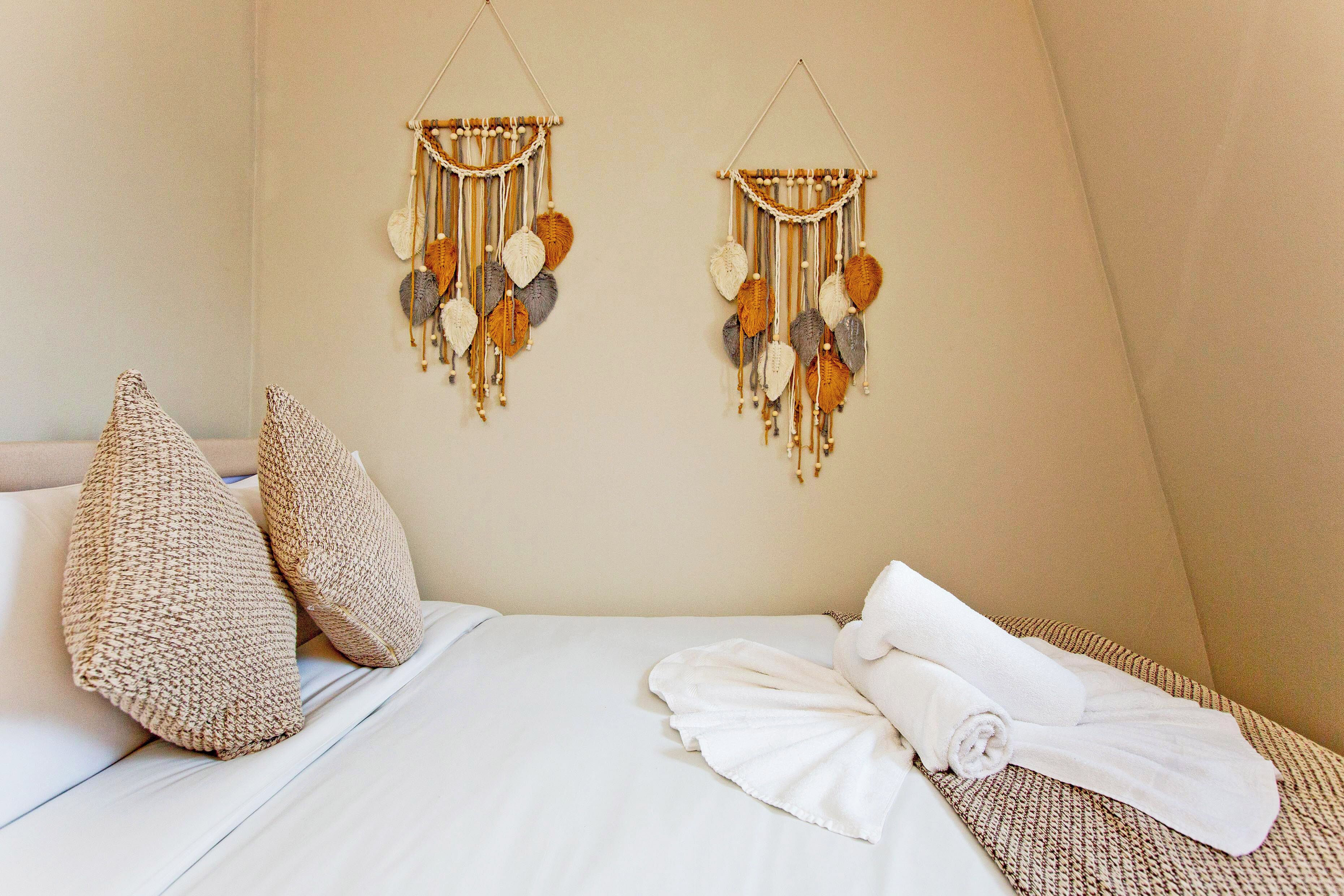 Un lit bien fait, avec une couette blanche, deux oreillers beige et une serviette blanche roulée posée sur le côté.