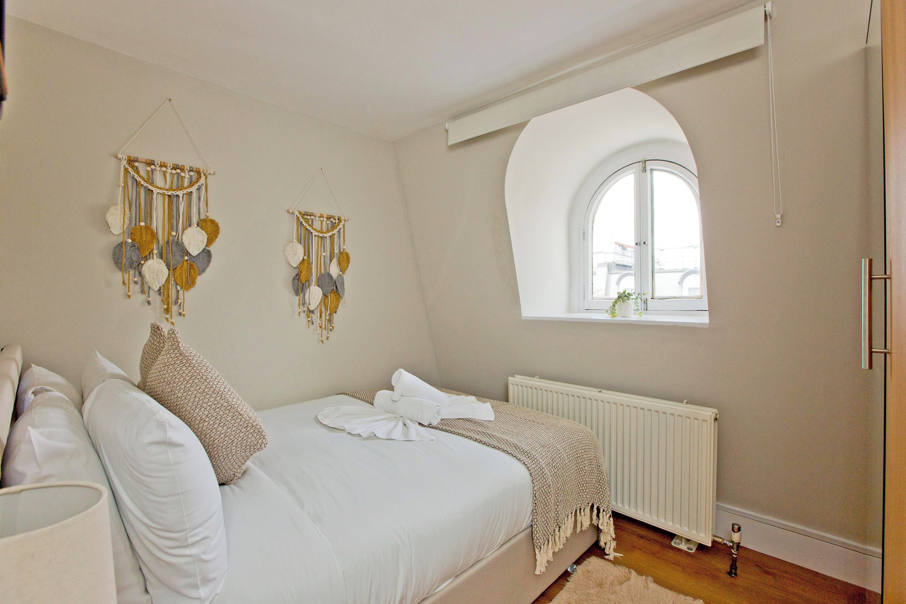 A bedroom with a large bed, a window with an arched design, and wall decorations.