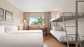 Quarto de hotel com duas camas, uma escrivaninha, uma cadeira, uma cama beliche e uma janela com vista para palmeiras.