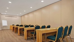 Uma sala de conferências com mesas compridas, cadeiras, um quadro branco e uma tela de projetor.