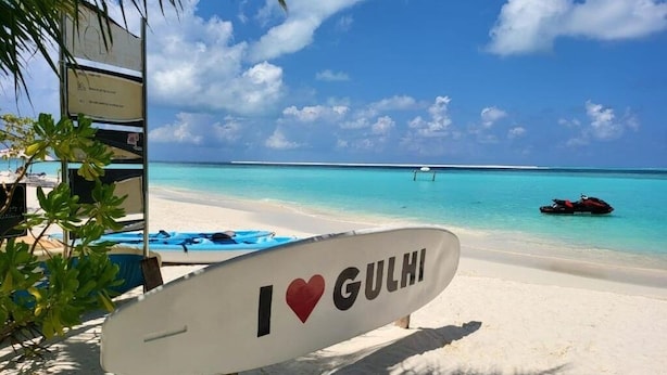 A beach scene with a surfboard sign that says "I ♥ GULHI" and a clear blue sky. - Ocean Pearl : Deluxe Double Room with balcony (Maafushi)