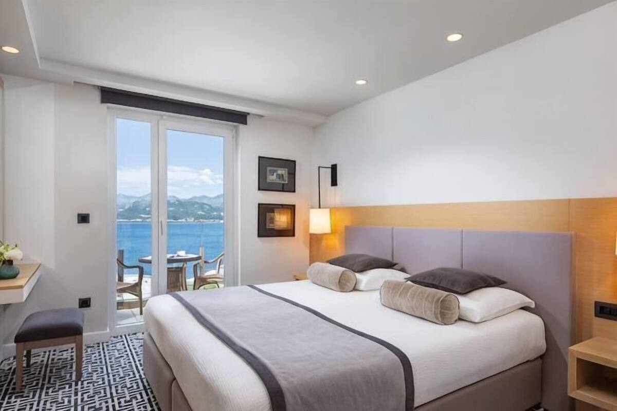 Habitación de hotel con cama, escritorio, silla, lámpara y vista al mar.