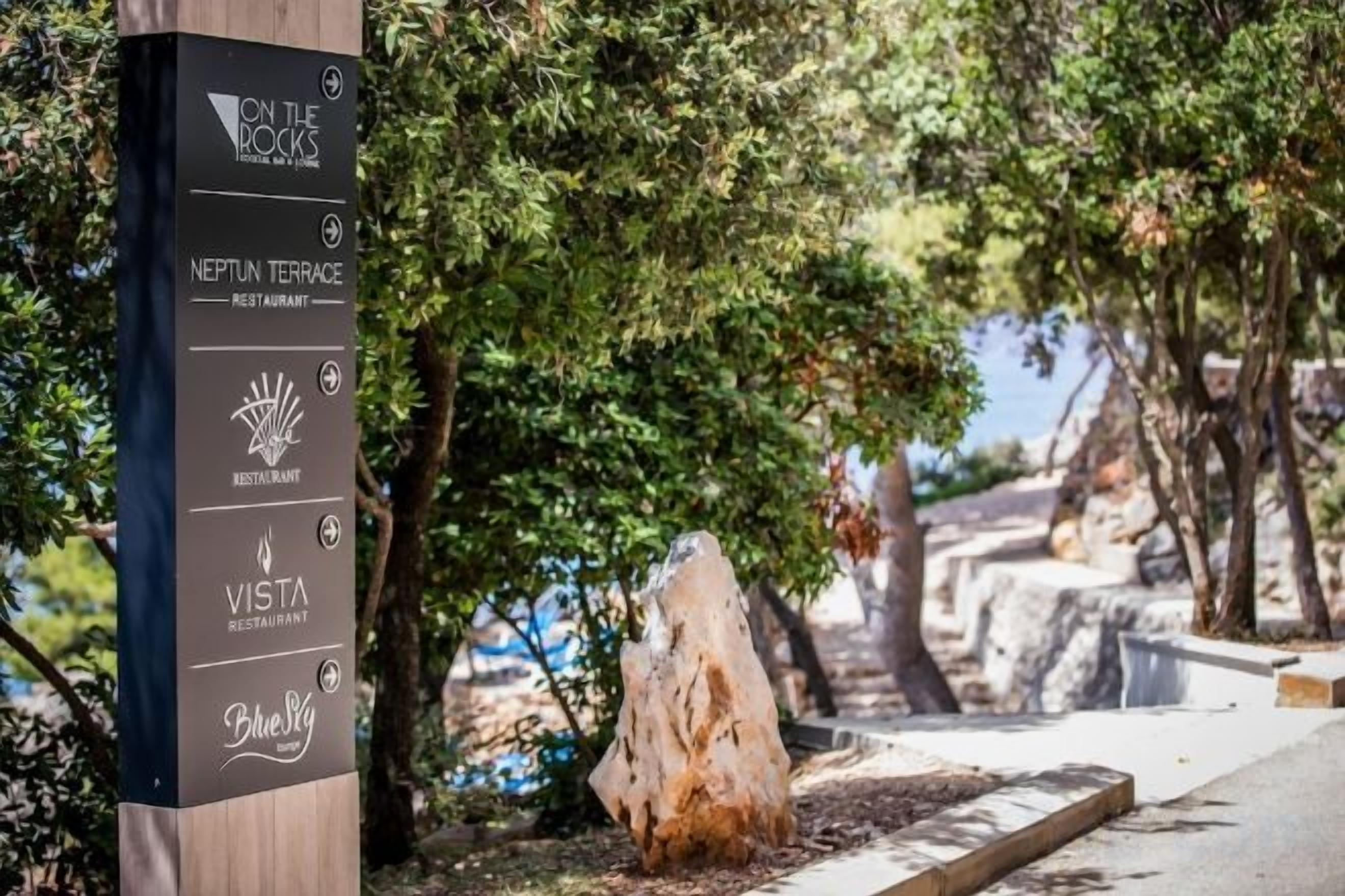 A signpost with restaurant names including 'On the Rocks,' 'Neptun Terrace,' 'Vesta,' and 'Blue Pig.'
