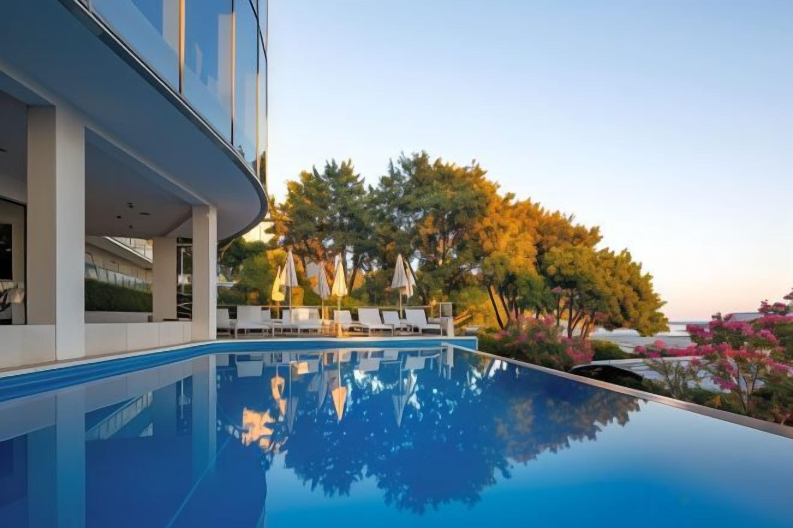 Un bâtiment moderne doté d’une piscine, de chaises longues et d’arbres.