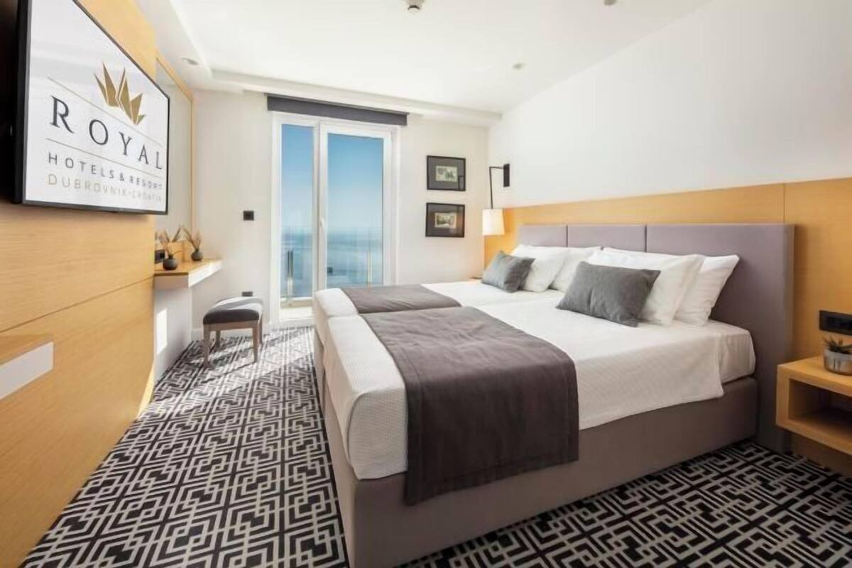 Habitación de hotel con cama, mesita de noche, silla, alfombra estampada y vista al océano.