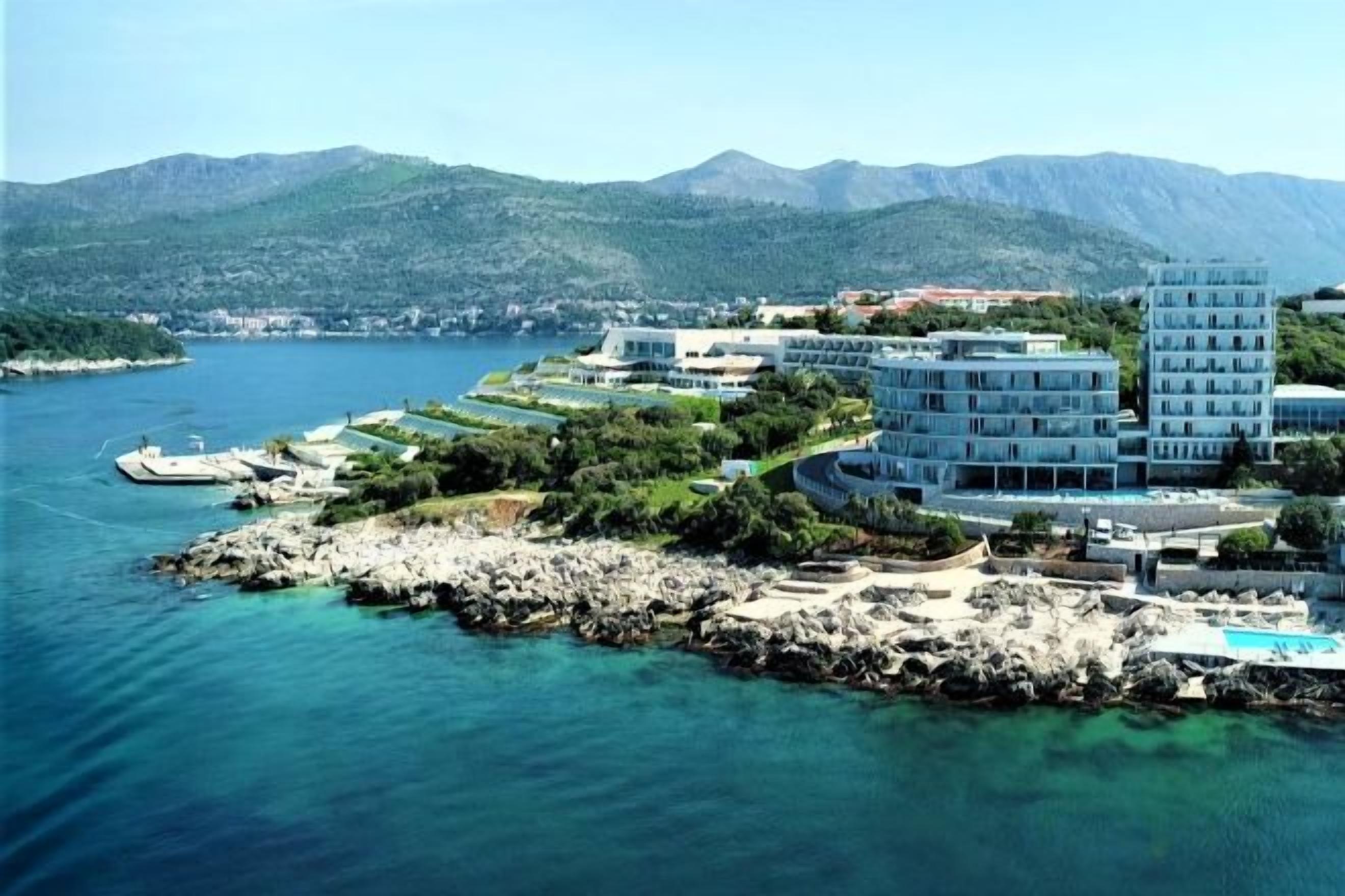 A coastal hotel with multiple buildings, a rocky shoreline, and a clear view of the sea.