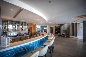 A bar area with a curved counter, seating, and a variety of bottles. - Royal Neptun Hotel (Dubrovnik)