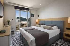 Una camera d'albergo con due letti, una scrivania, una sedia, una lampada e vista sull'esterno.