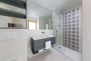 Un bagno moderno con cabina doccia in vetro, mobile lavabo bianco e uno specchio grande.