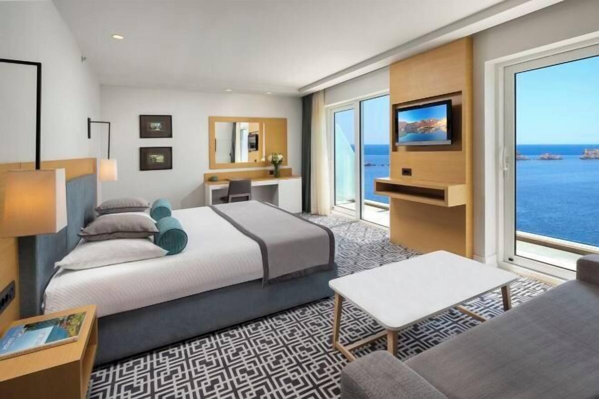 Un hotel moderno con una cama grande, un escritorio, una silla, un televisor y vista al mar.