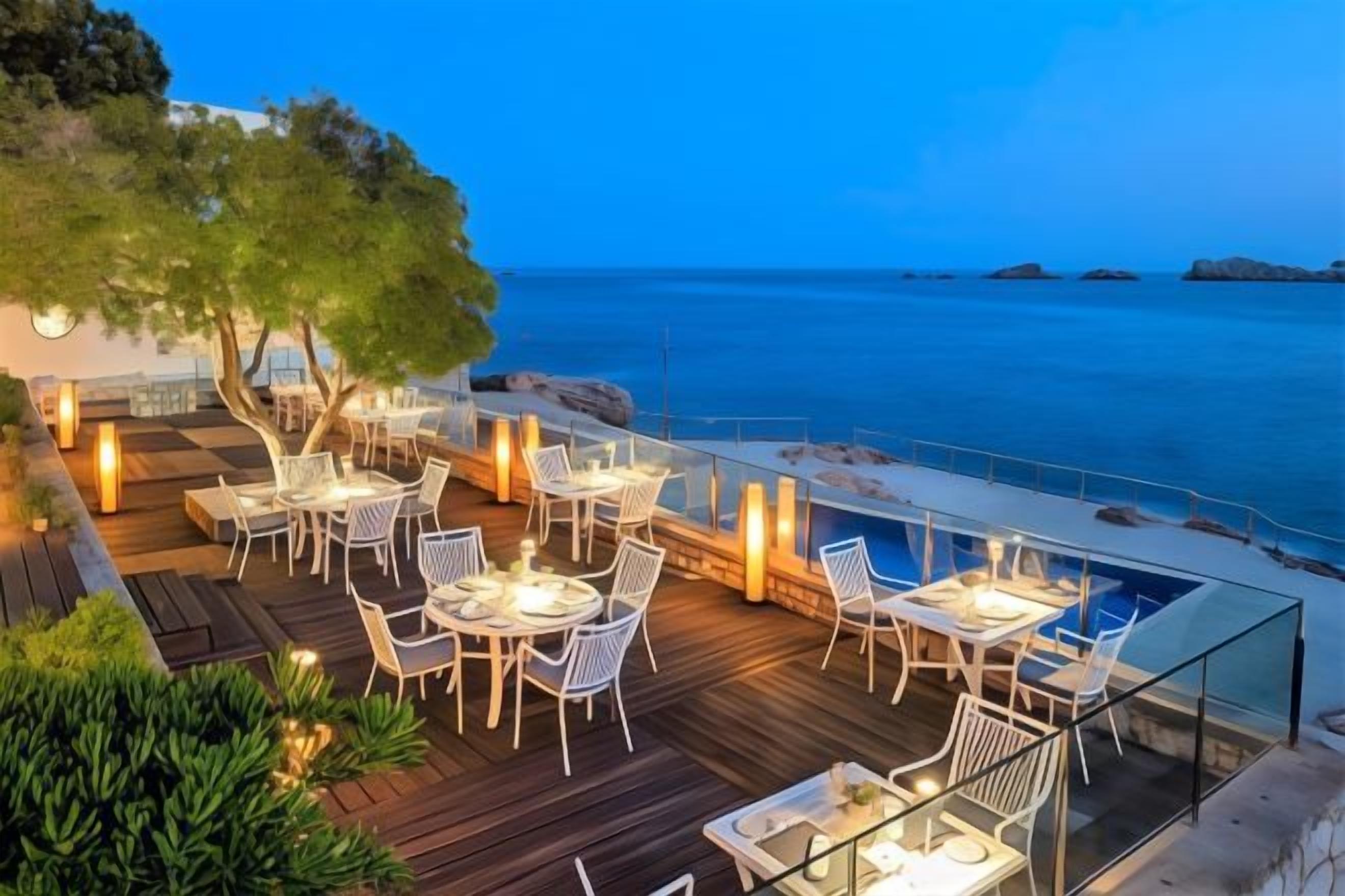 An outdoor dining area with tables and chairs, overlooking a body of water.