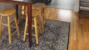 Une cuisine compacte avec des meubles de couleur sombre, un four à micro-ondes et un réfrigérateur. On y trouve une table à manger avec deux tabourets et un tapis à motifs.