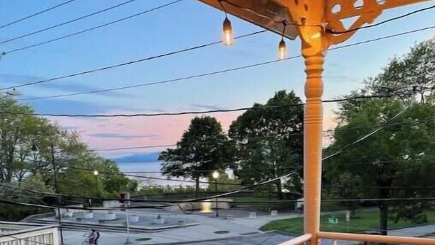 Un balcon donnant sur une route et des arbres, agrémenté d’une balustrade et d’une pergola illuminée.