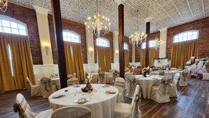 A banquet hall with round tables, white chairs with bows, and chandeliers.