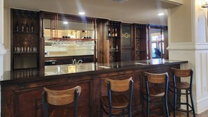 A bar area with a dark wooden bar counter, three bar stools, and a mirrored backsplash.