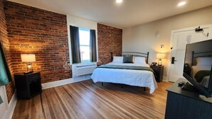 A bedroom with a brick wall, a bed, a TV, and a window.