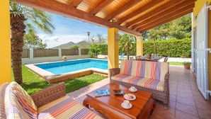 Eine überdachte Terrasse mit Pool, Korbmöbeln und Bergblick.
