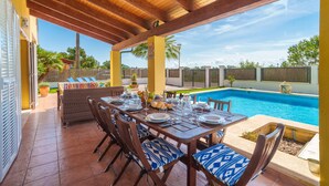 Eine Außenpatio mit Pool, Holztischen und -stühlen sowie einem überdachten Sitzbereich.
