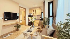 Una sala moderna con un televisor de pantalla plana, una mesa de comedor y un sofá. Cuenta con una zona de cocina con armarios de madera y un refrigerador.