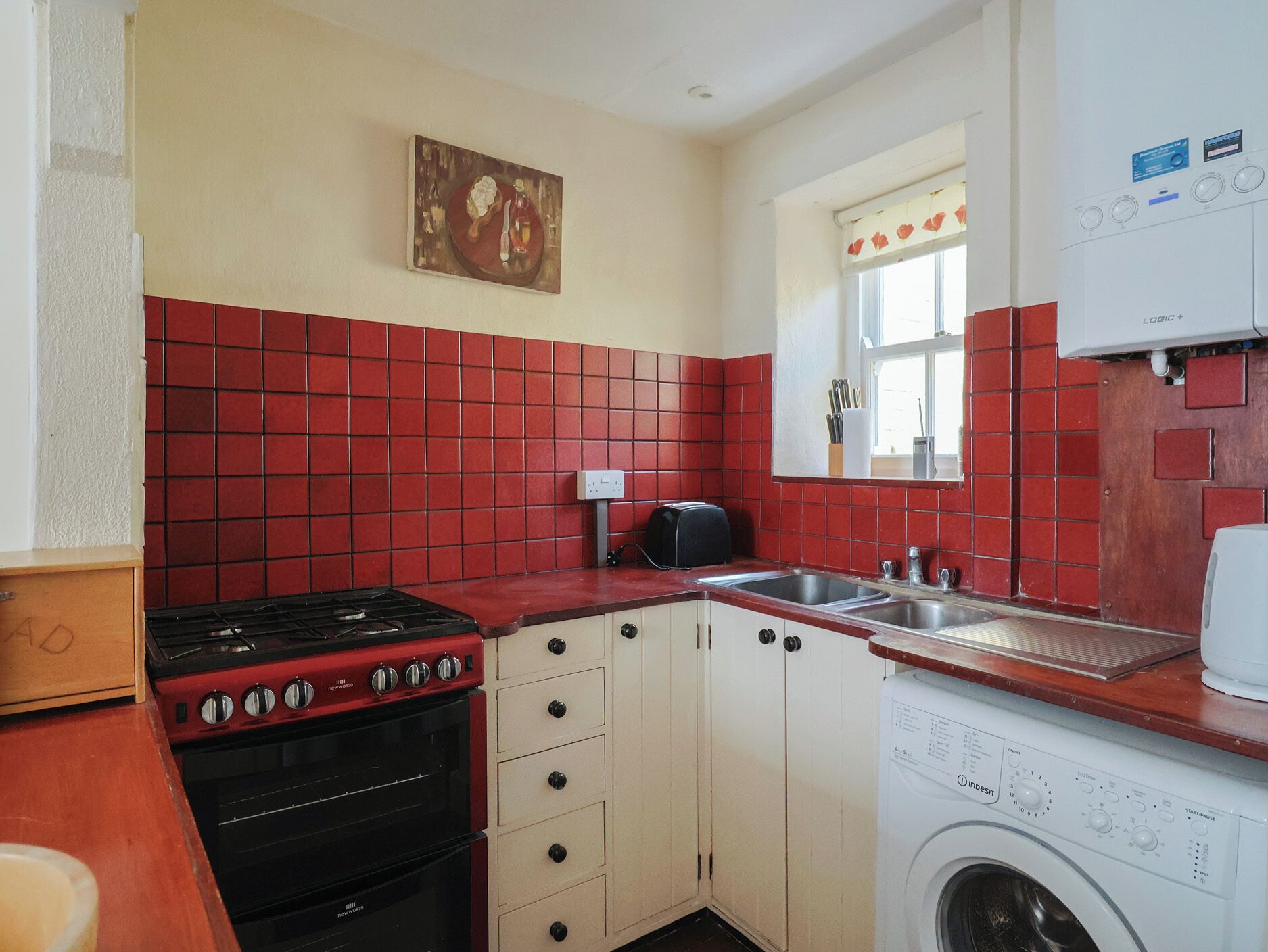 A compact kitchen with a red-tiled backsplash, a stove, a sink, and a washing machine.