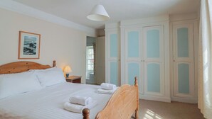 Een slaapkamer met een houten bed, witte lakens, een bedlampje, een ingelijste foto aan de muur, en een paar lichtblauwe deuren.