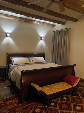 A bedroom with a wooden bed, a bench, a patterned rug, and two wall-mounted lights.