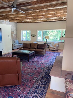 A spacious living room with a large rug, leather sofas, and a ceiling fan.