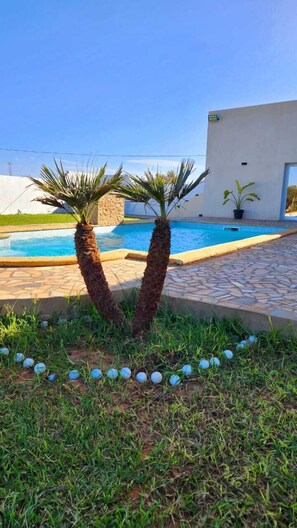 A swimming pool with palm trees in the foreground and a modern building in the background. - Casa Firma (Korba)