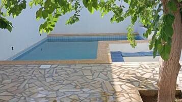 Zona de piscina con suelo de piedra y un árbol en primer plano.