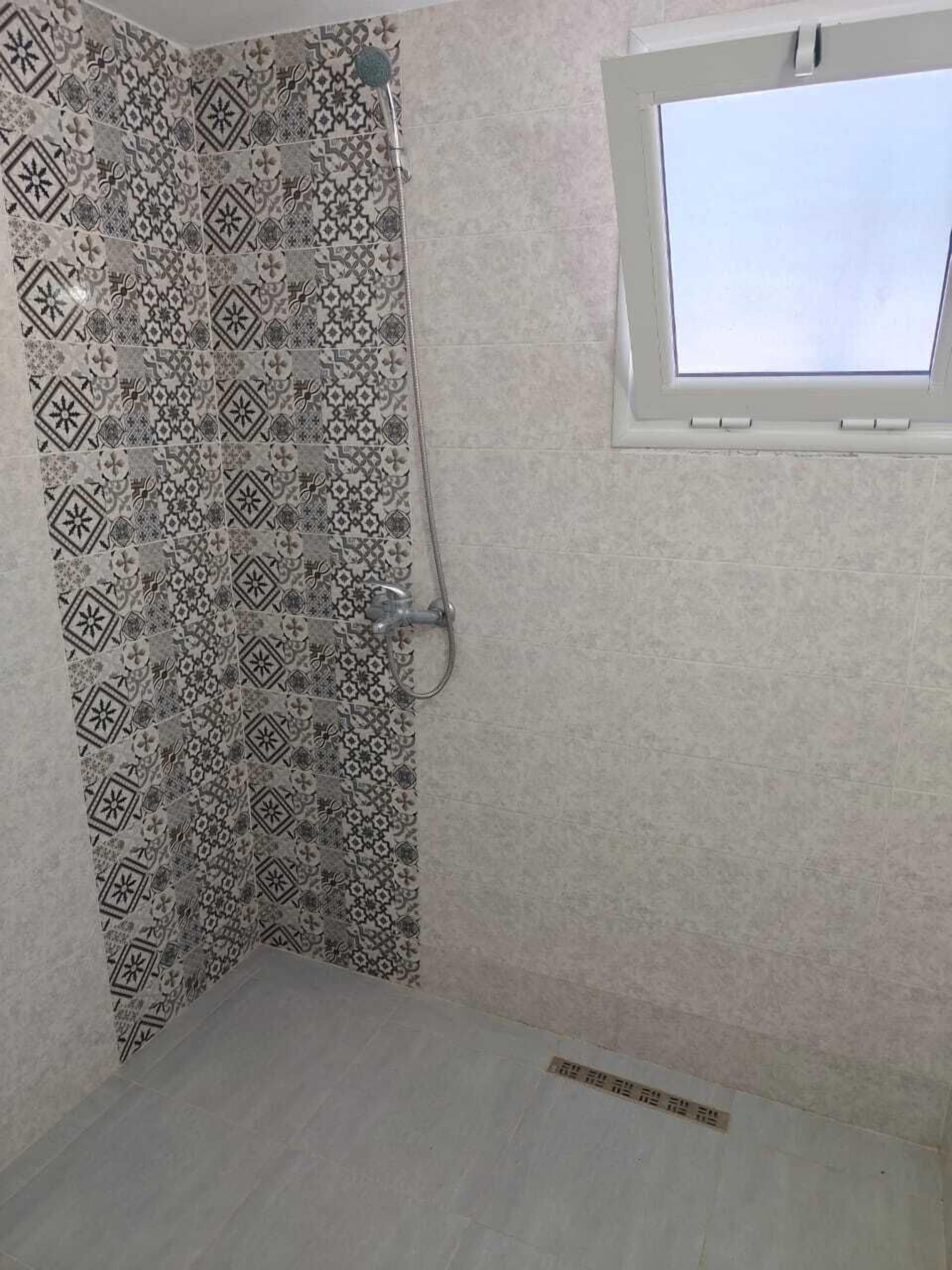 Bagno con piastrelle decorate, doccia e finestra sul tetto.