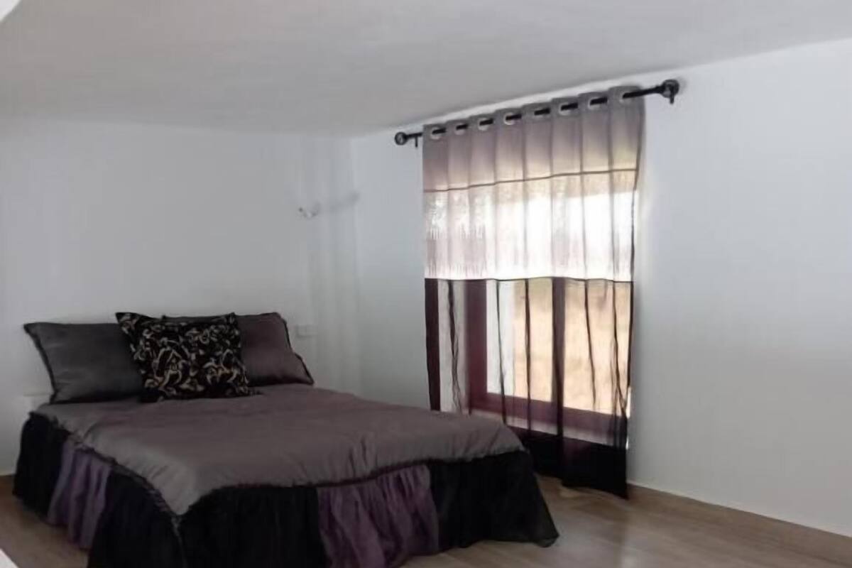 A bedroom with a bed, a window with curtains, and a wooden floor.