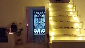 Uma escadaria iluminada conduz a um ambiente com piso xadrez e uma porta com design geométrico.