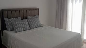 Ein Einzelbett mit Kopfteil, weißer Bettwäsche und gestreifter Kopfkissen.