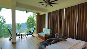 A bedroom with a bed, a chair, a table, and a view of the outdoors. - Roots Munnar (Devikolam)
