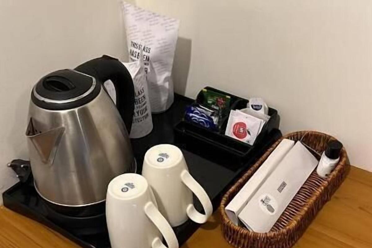 Egy konyhapult, rajta egy kávéfőző, két fehér bögre, egy palackot tartalmazó kosár, és egy tálca, amelyen egy doboz és egy zacskó található.