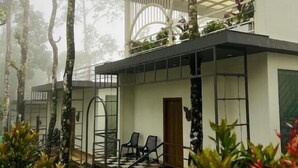 A modern building with a glass balcony, surrounded by trees and plants. - Roots Munnar (Devikolam)
