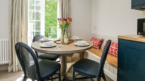 A dining area with a round table, four chairs, a vase with flowers, and a view of greenery outside. - Cedar (Newbury)