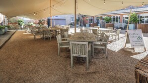 An outdoor seating area with wooden tables and chairs, string lights, and a sign advertising coffee, cakes, and toastsies. - Cedar (Newbury)