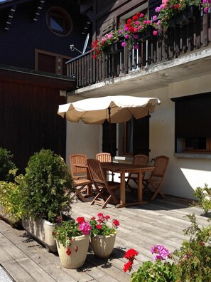 Um deck de madeira com mesa e cadeiras, rodeado por vasos com plantas e flores.